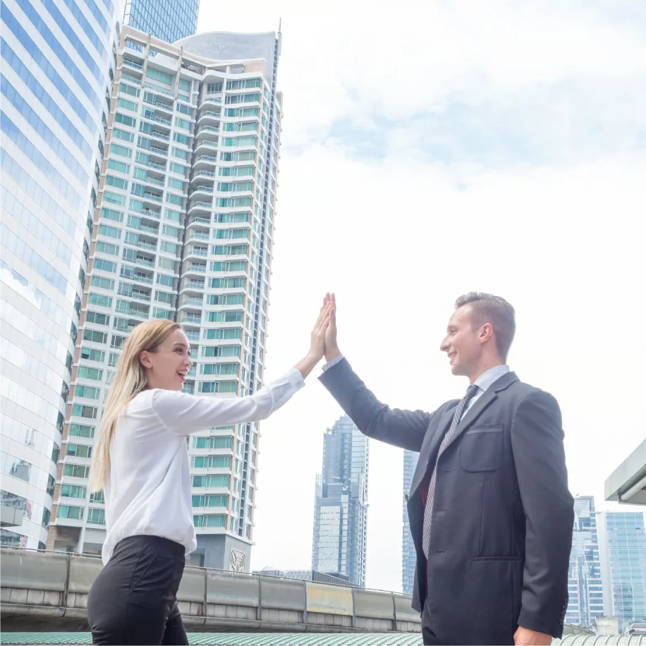 Zwei Geschaeftsleute geben sich vor einem Buero ein High Five um ihren Erfolg zu feiern
